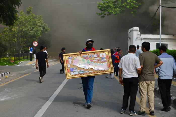 Un manifestante camina con un mapa enmarcado de Nepal mientras entra en el Singha Durbar, el principal edificio administrativo del gobierno nepalí, en Katmandú el 9 de septiembre de 2025, un día después de la represión policial contra las manifestaciones por la prohibición de las redes sociales y la corrupción gubernamental.