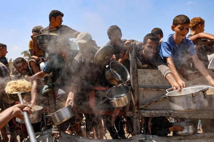 Hombres y niños palestinos extienden sus ollas vacías para recibir arroz cocido de una cocina benéfica en la Ciudad de Gaza.