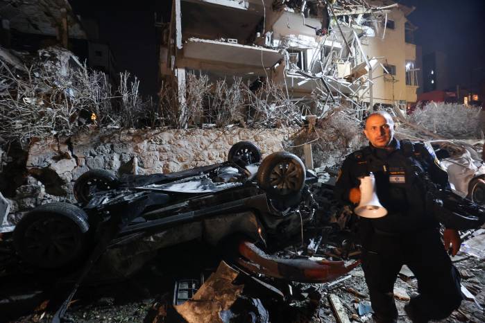 Un miembro de las fuerzas de seguridad israelíes pasa junto a un auto destruido en un sitio impactado por un misil disparado desde Irán, en Ramat Gan, en las afueras de Tel Aviv.