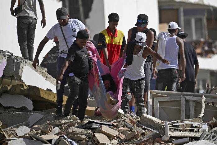 Varias personas transportan a una mujer sobre una manta entre los escombros de un edificio de apartamentos dañado tras el terremoto en Catia La Mar, estado de La Guaira, a unos 30 km al noroeste de Caracas, el 25 de junio de 2026.