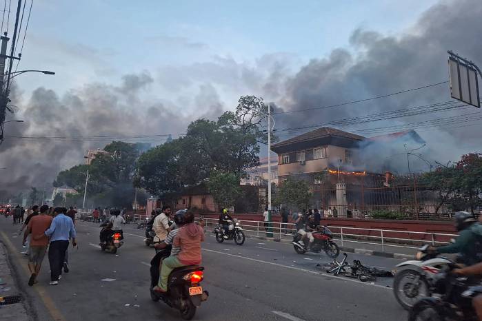 Los pasajeros pasan junto al edificio del Tribunal Supremo en llamas, incendiado por manifestantes en Katmandú el 9 de septiembre de 2025, un día después de la represión policial contra las manifestaciones por la prohibición de las redes sociales y la corrupción gubernamental.