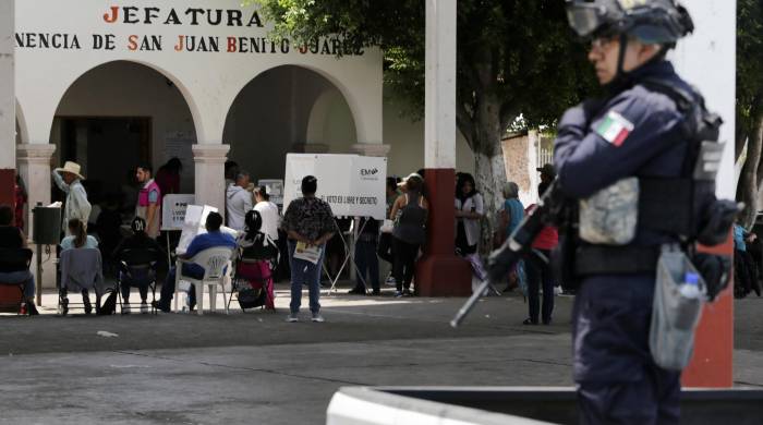 La gente vota mientras miembros de la Policía de Michoacán custodian una mesa electoral.