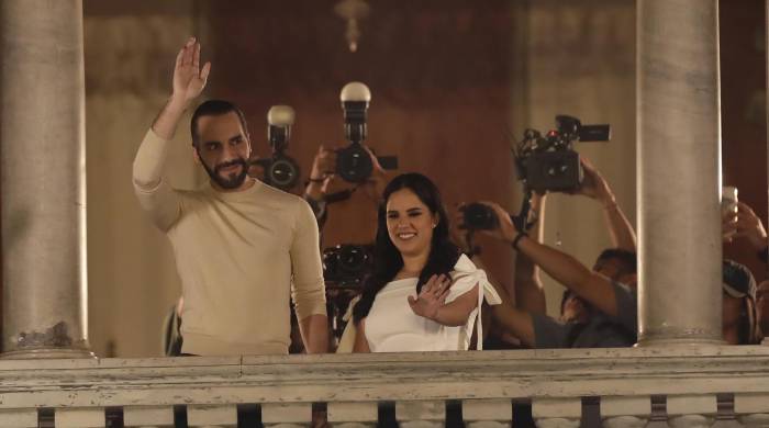 El actual presidente y ganador de la reelección en El Salvador, Nayib Bukele, saluda desde el Palacio Nacional junto a su esposa Gabriela Rodríguez de Bukele.