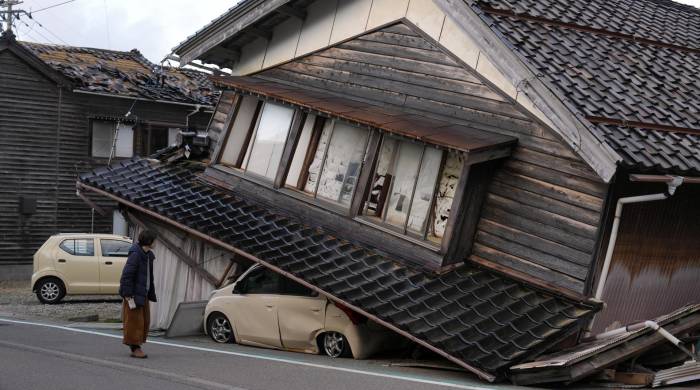 Una mujer observa una vivienda y vehículos dañados tras un fuerte terremoto en Tohi Town, en la península de Noto, Japón, este 2 de enero de 2024.