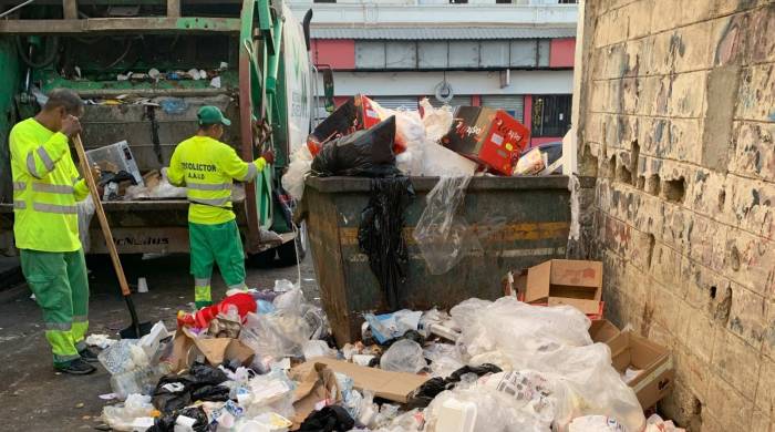 Una estampa urbana común estos días. En la imagen se aprecia una gran cantidad de basura acumulada en la calle, incluyendo plásticos, cartones, envases, y otros desechos. Hay un contenedor de basura metálico que está desbordado y la basura se extiende desde este punto a lo largo del suelo.
