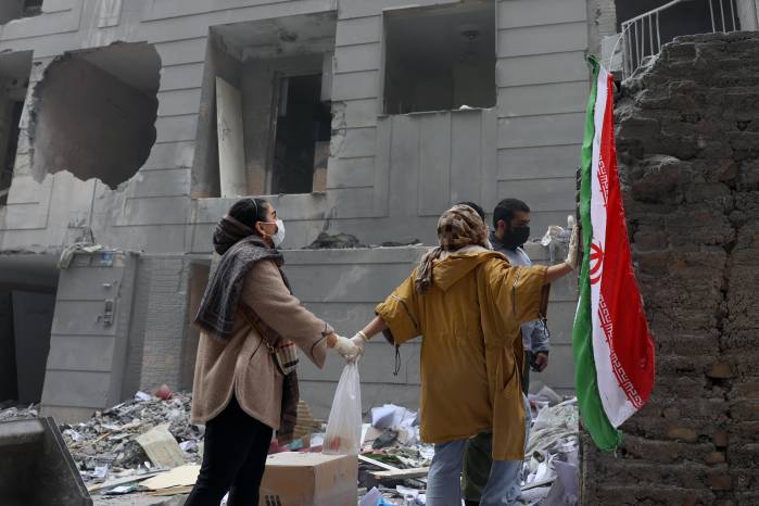 Dos hermanas iraníes se dan la mano frente a un edificio dañado en el sur de Teherán, Irán, el 15 de marzo de 2026.