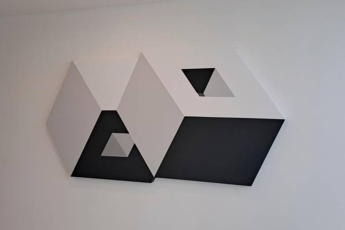 En esta obra, son los mismos códigos de 2014, ahora en movimiento. Ya no están sobre el lienzo; están hechos sobre aluminio.